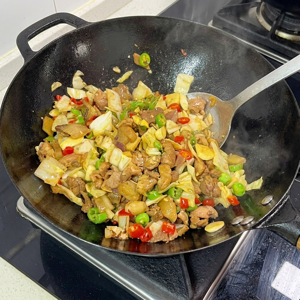 Una spatola di metallo che salta attivamente crauti, maiale a fette e peperoncini tritati insieme in un wok fumante.