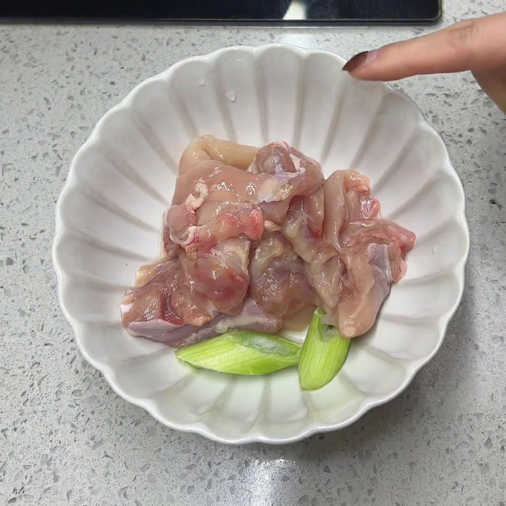 Sovracosce di pollo disossate e pezzi di cipollotto in una ciotola bianca.