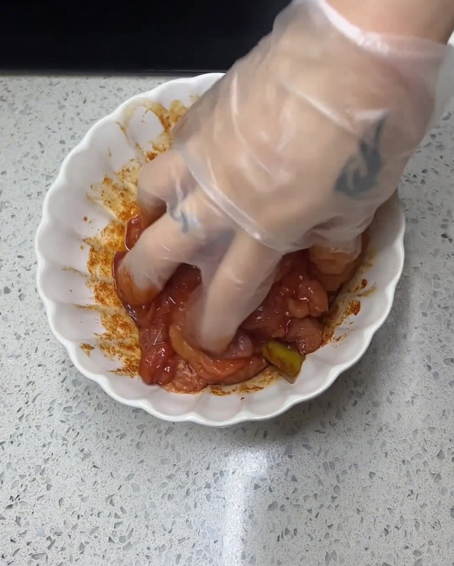 Una mano guantata massaggia la marinata speziata sul pollo crudo.