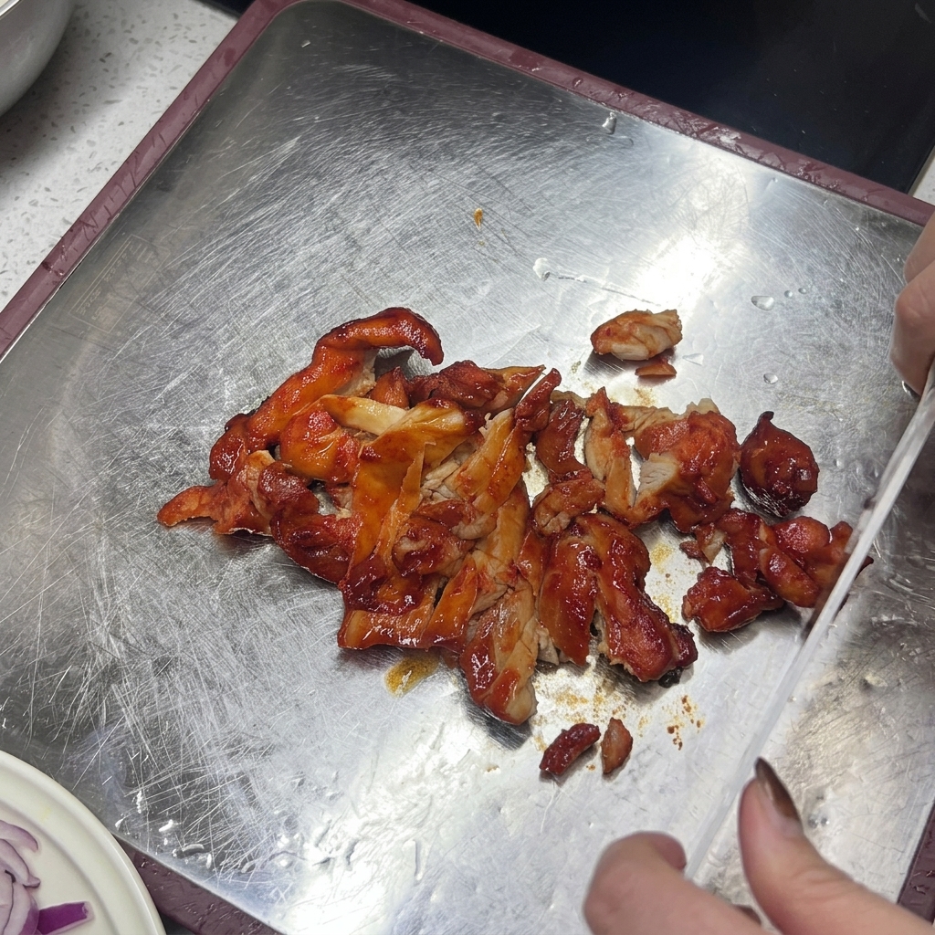 Un coltello affetta il pollo glassato cotto su un tagliere metallico.