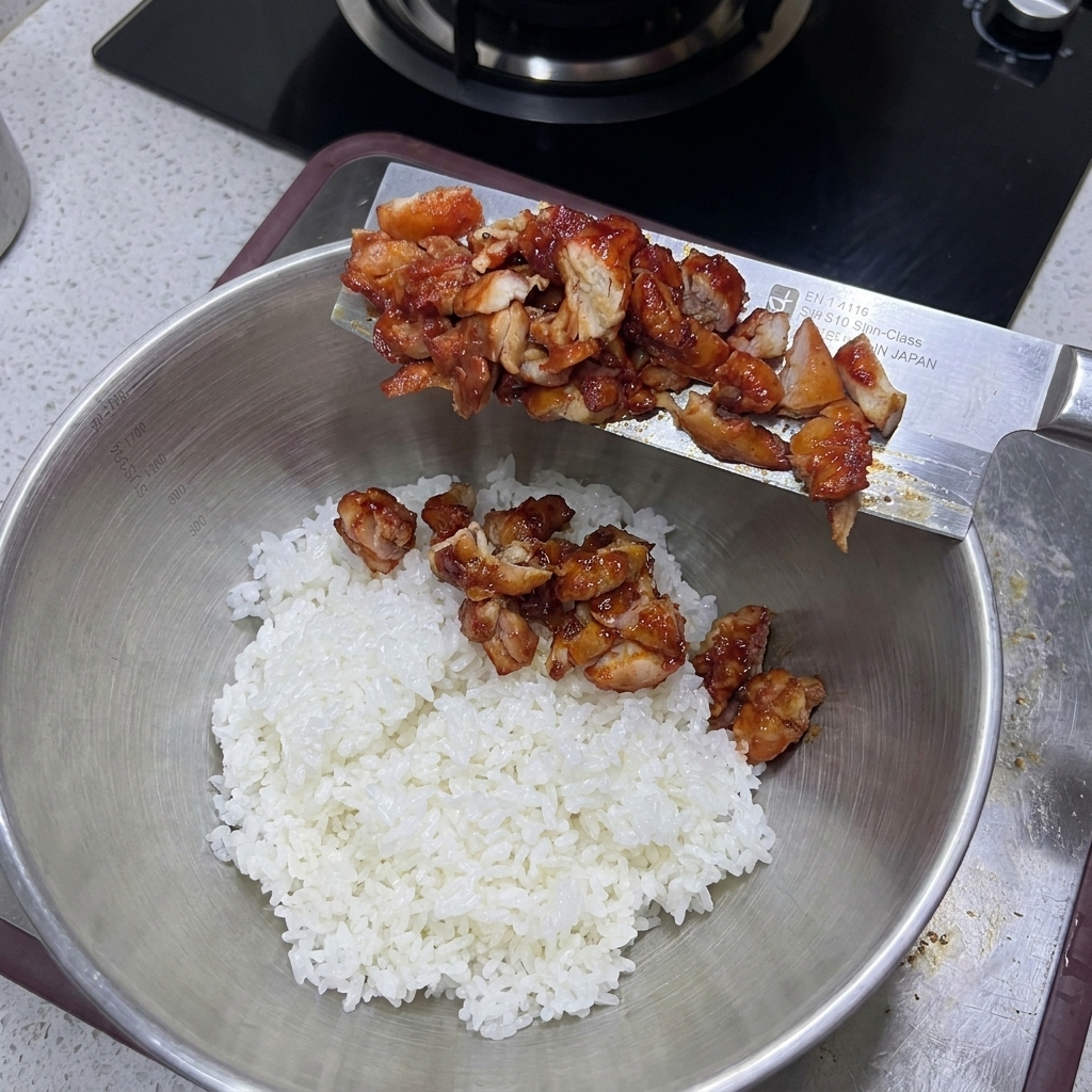Il pollo cotto a pezzi viene versato da un coltello in una ciotola di riso bianco.