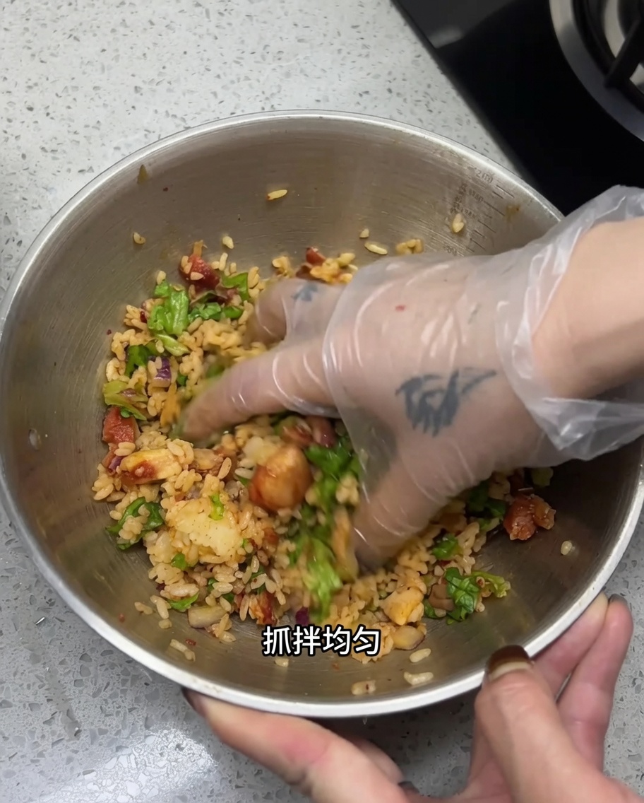 Una mano guantata mescola tutti gli ingredienti in una ciotola di acciaio.