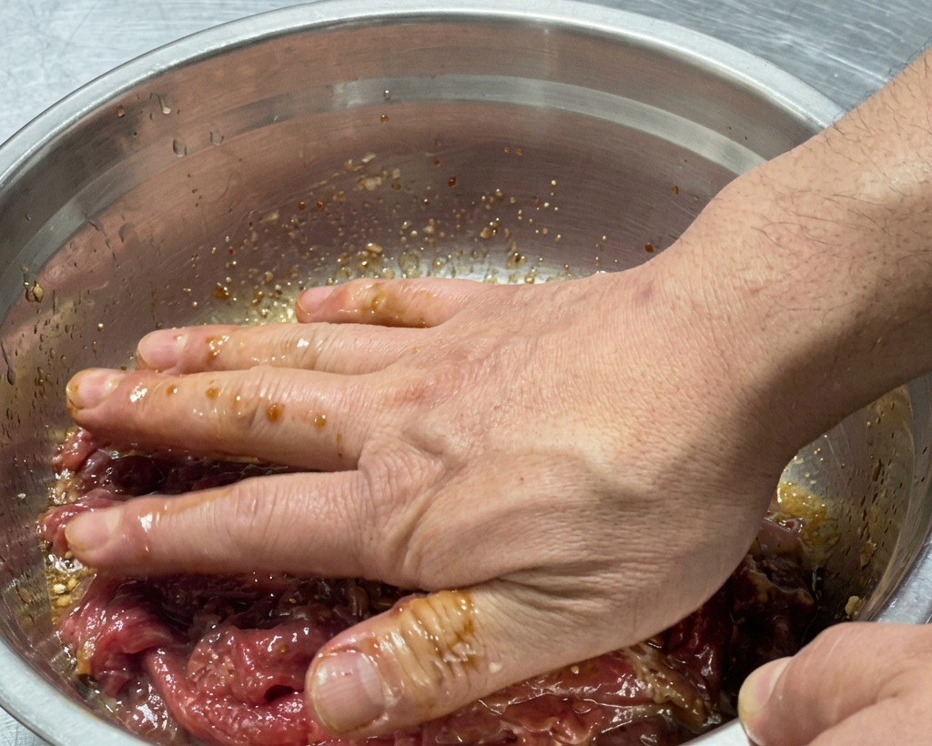 Mani che mescolano accuratamente il manzo crudo con la marinata nella ciotola.