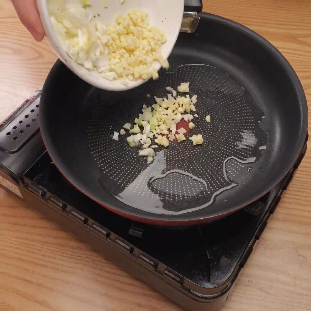Cipolla tritata, cipollotto e aglio che sfrigolano in una padella calda con olio.