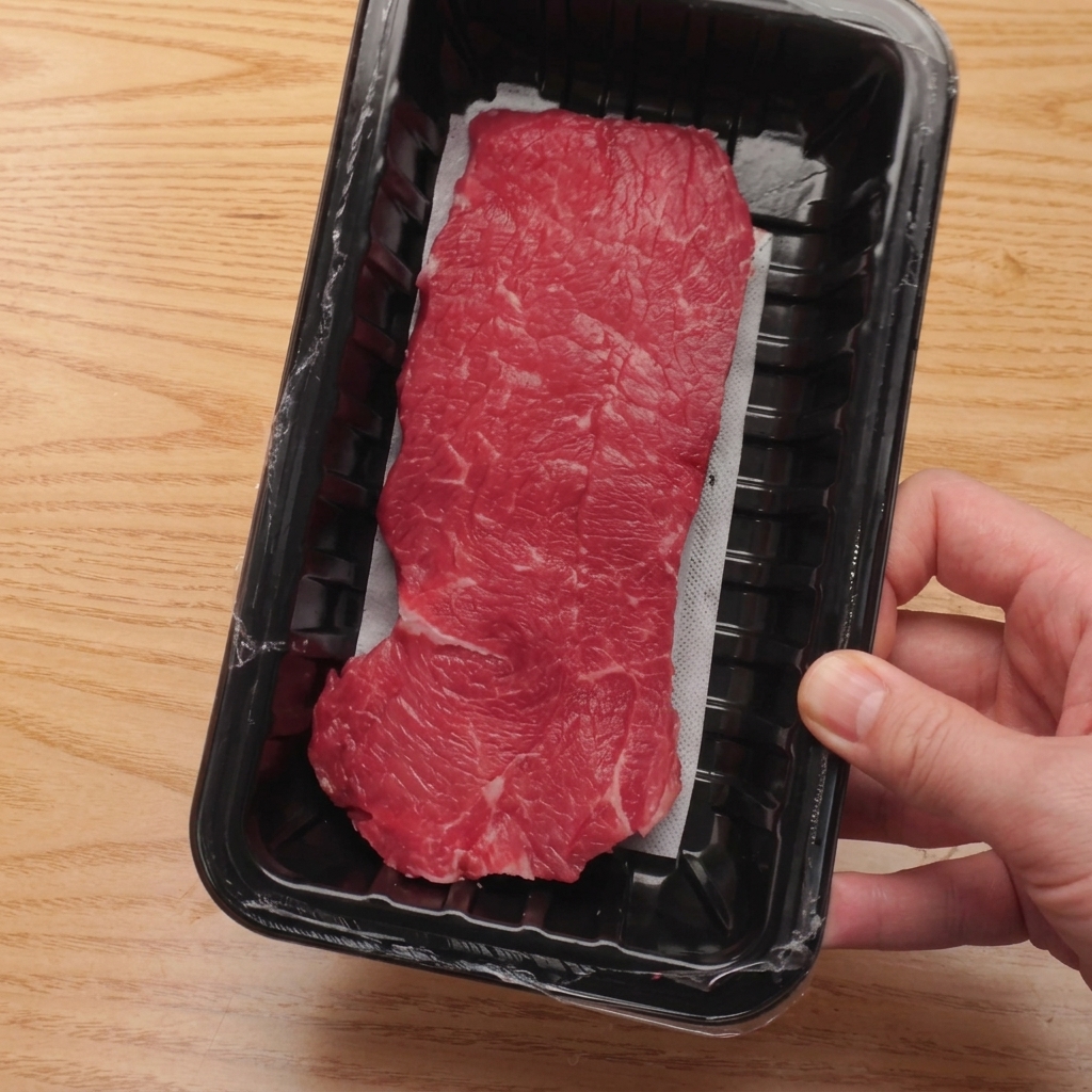 Controfiletto di manzo crudo tagliato in cubetti uniformi su un tagliere di legno.