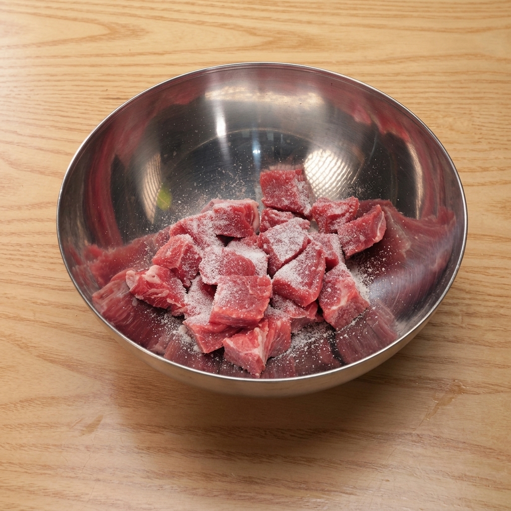 Cubetti di manzo in una ciotola di metallo conditi con sale, zucchero, salsa di soia e amido.