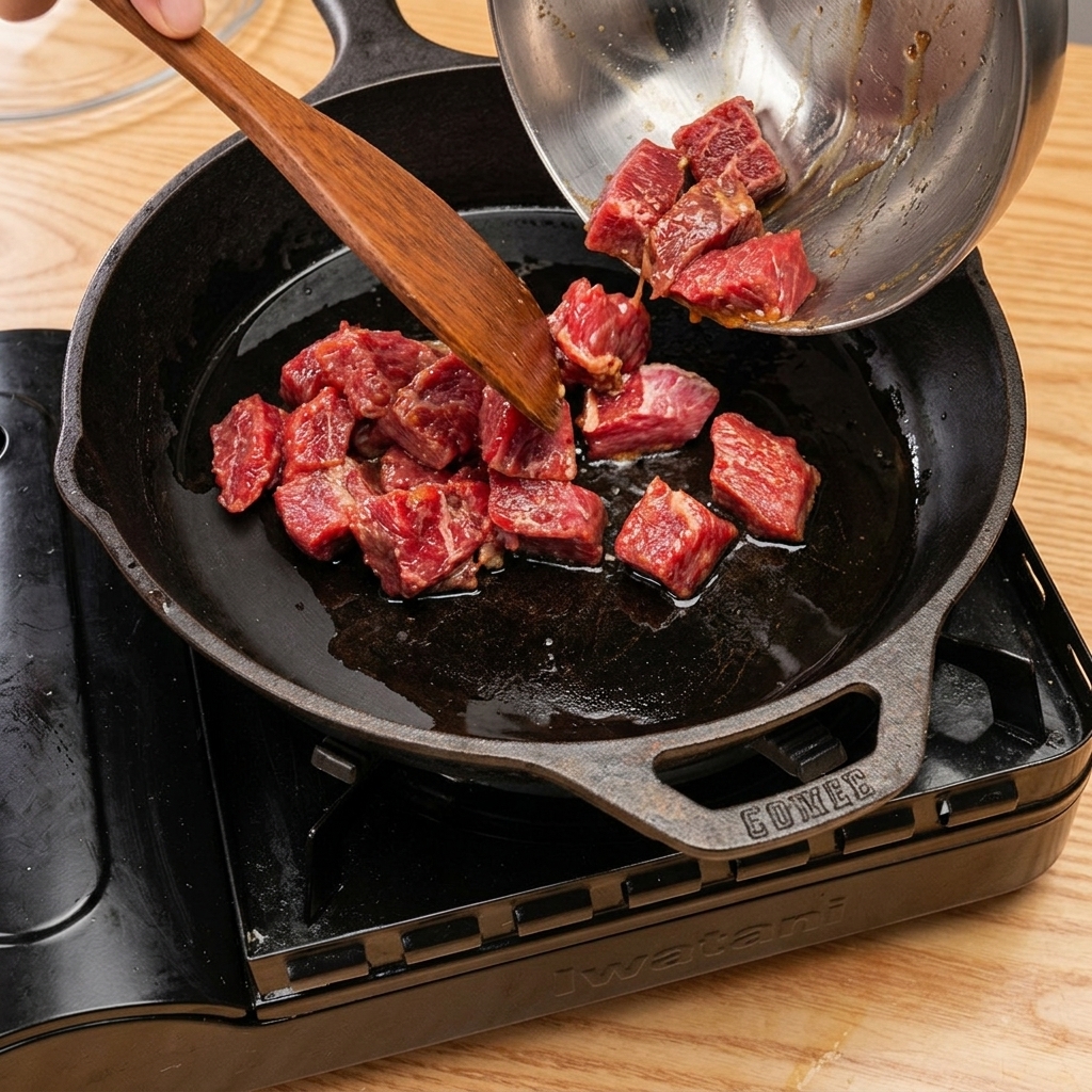 Cubetti di manzo che rosolano in una padella di ghisa, con vapore che si sprigiona dopo laggiunta di vino da cucina.