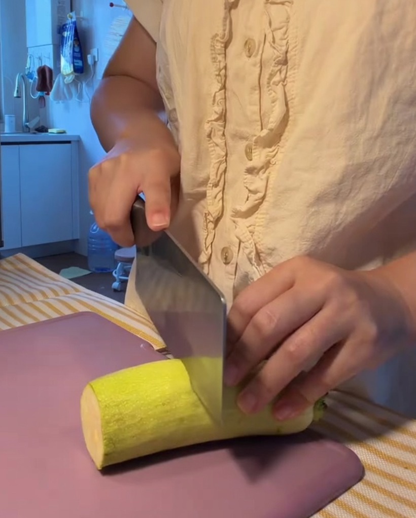 Zucchina fresca tagliata a fettine semicircolari su un tagliere viola.