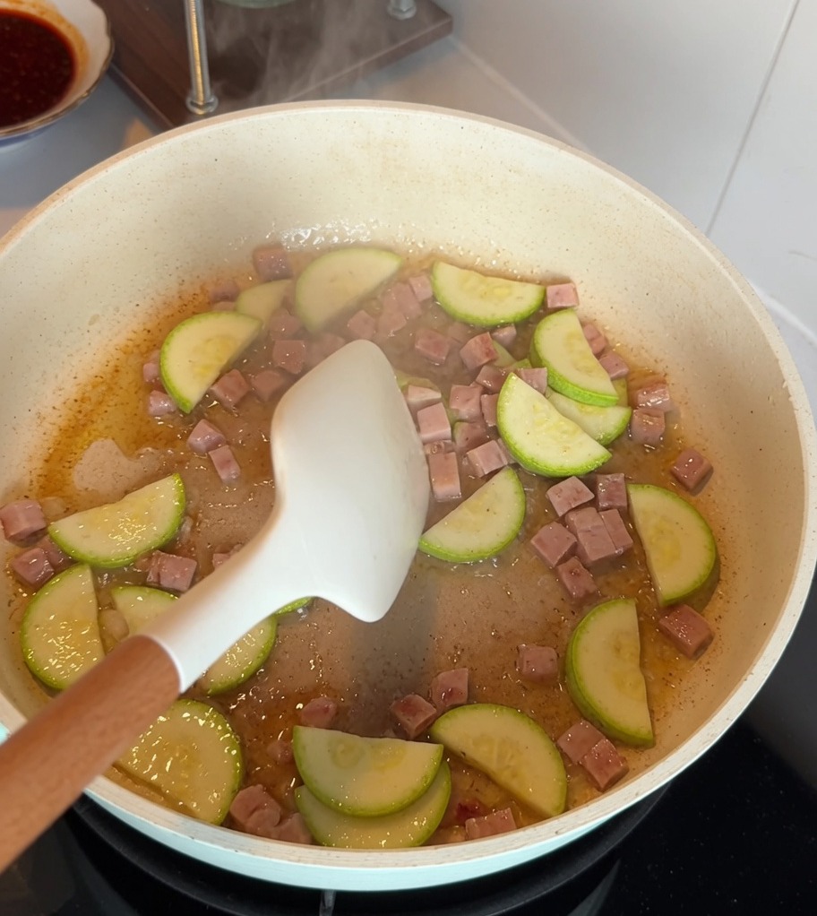 Fette di zucchina e cubetti di carne in scatola saltati insieme in una padella antiaderente.