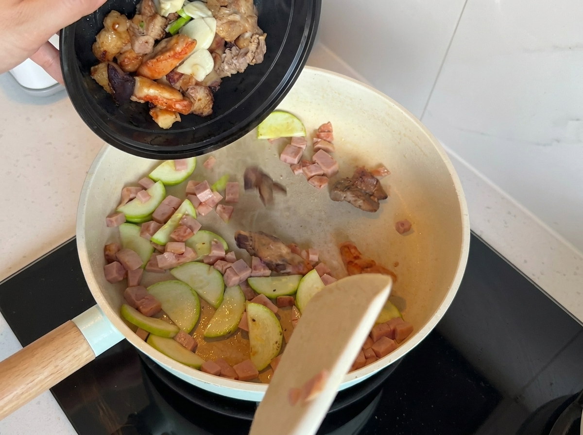 Una padella contenente zucchine e carne saltate con laggiunta di cipollotti, aglio e pezzi di carne precotta.