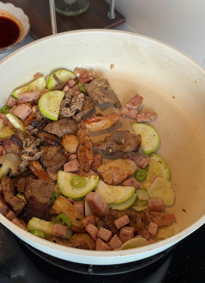Uova sbattute mescolate con zucchine e carne in una padella bianca.