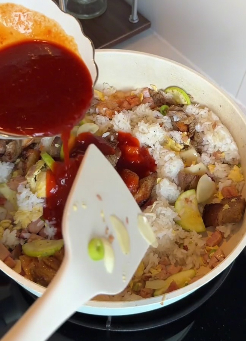 Salsa bibimbap versata sul riso e sugli ingredienti in una padella.