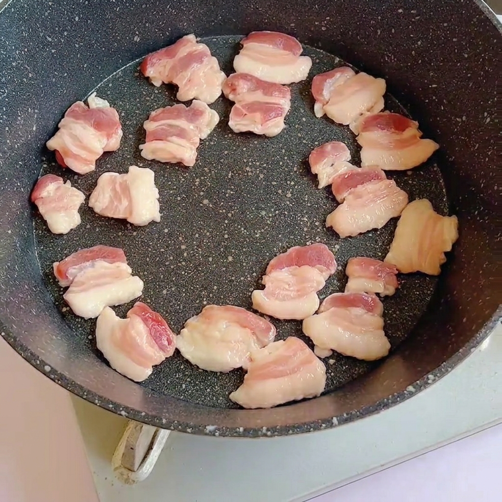 Fette di pancetta cruda disposte in una padella calda che iniziano a rosolare.
