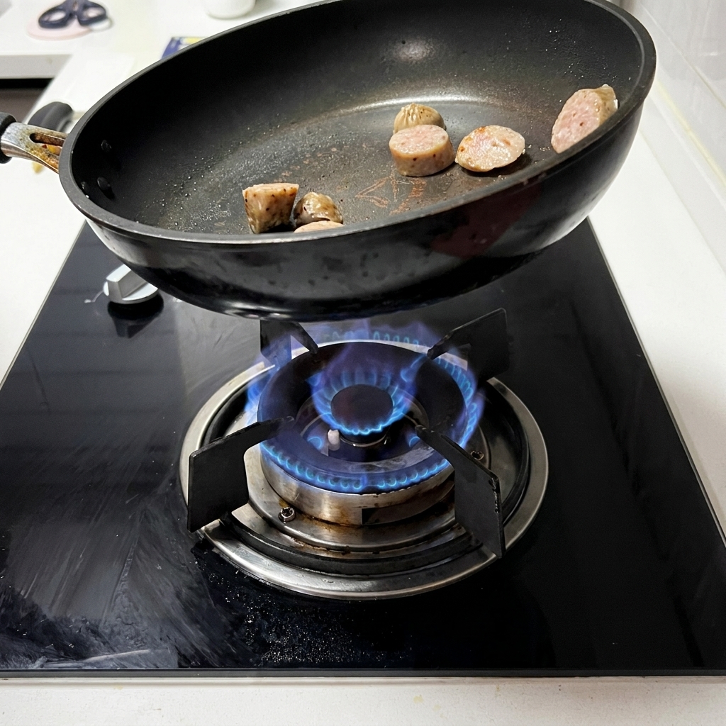 Fette di salsiccia che sfrigolano e rosolano in una padella nera su un fornello a gas.