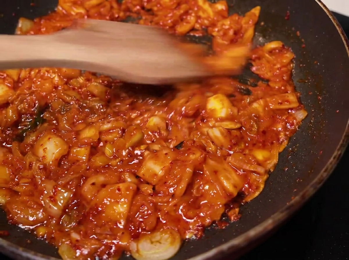 Il composto di kimchi mescolato e cotto in padella con una spatola di legno.