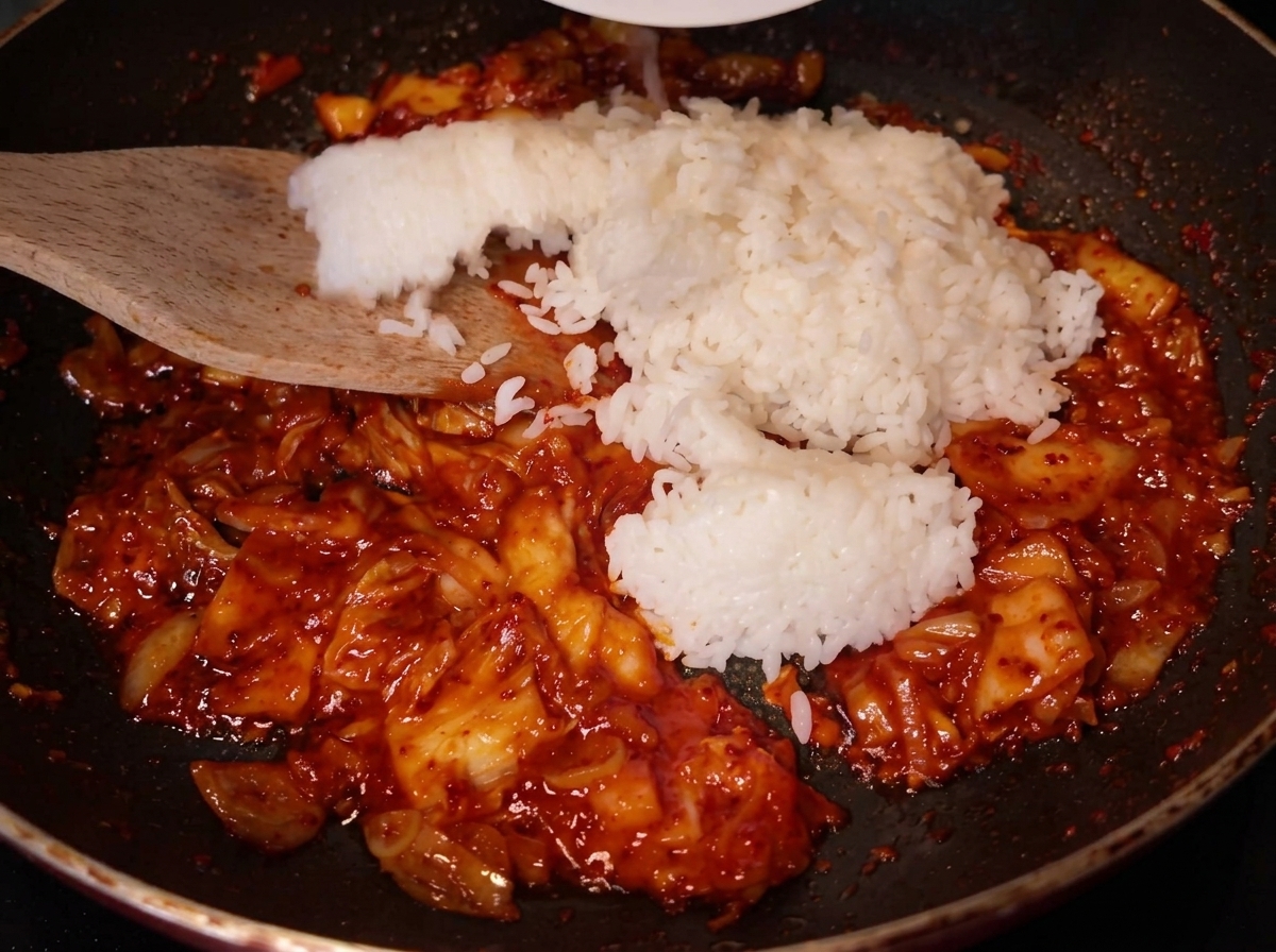 Una spatola di legno che aggiunge una porzione di riso bianco nella padella con il kimchi.