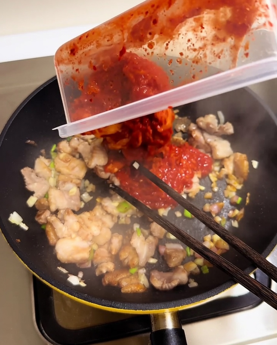 Kimchi rosso tritato versato da un contenitore nella padella con carne e aromatici.