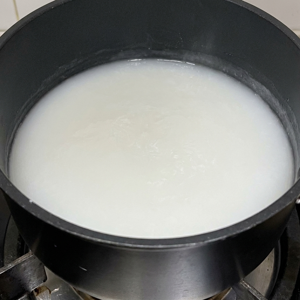 Una densa pasta bianca di farina di riso glutinoso che cuoce in una pentola nera.