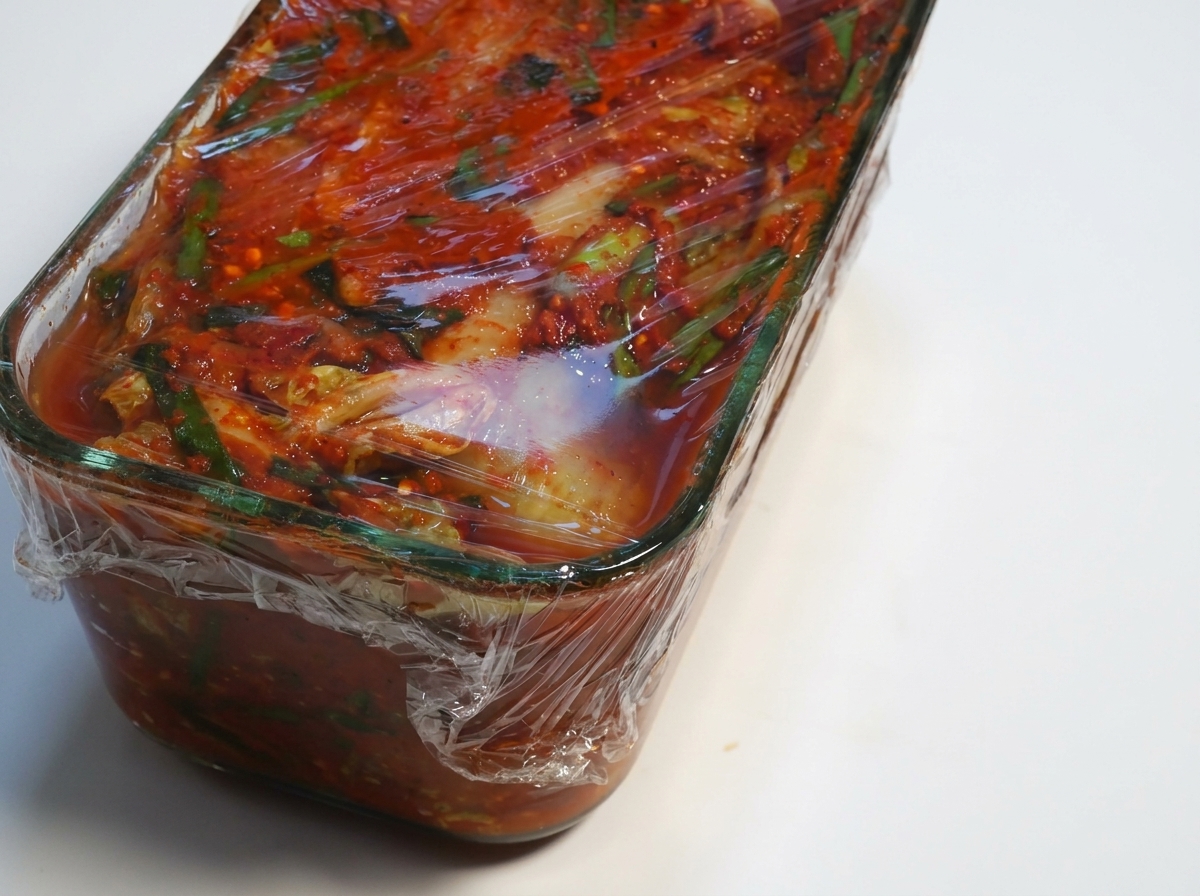 Contenitore di kimchi fermentato con la pellicola trasparente che viene rimossa.