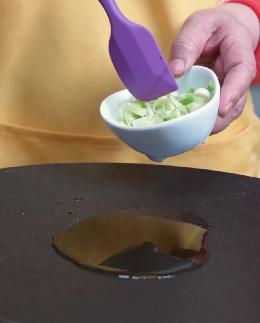Cipollotti tritati che soffriggono in padella con olio di sesamo.