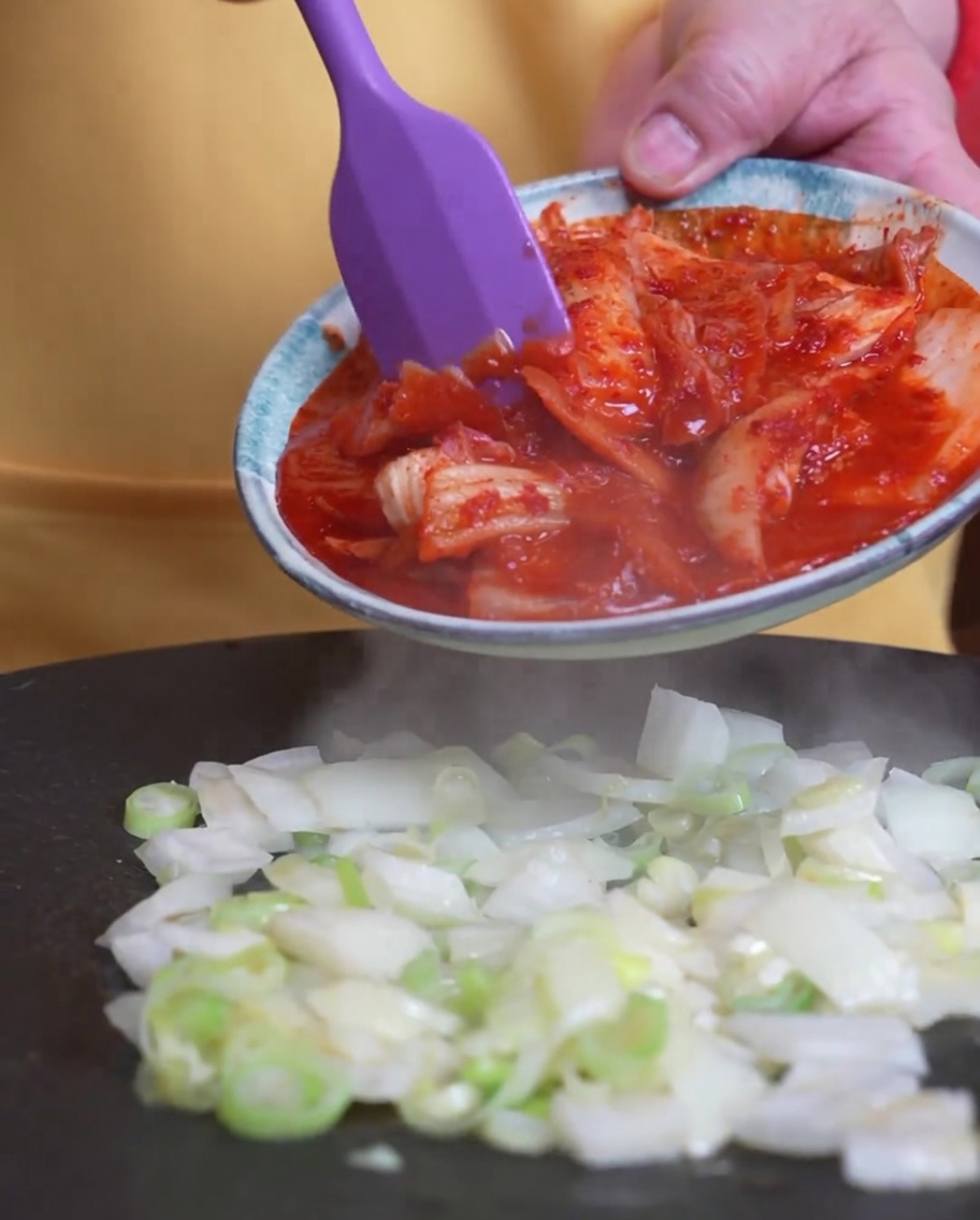 Il kimchi aggiunto nella padella insieme ai cipollotti in cottura.