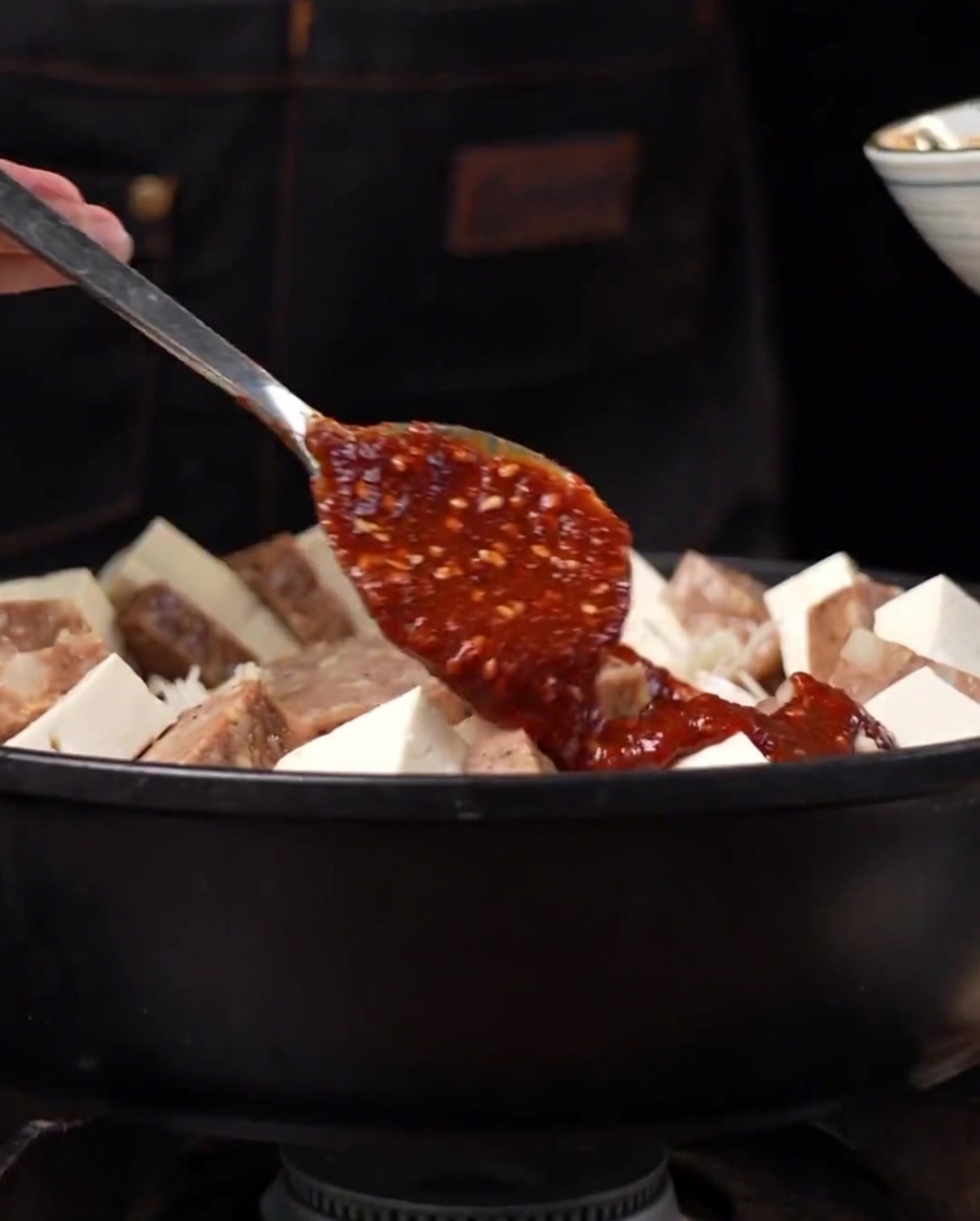 Una salsa piccante densa e rossastra distribuita sopra gli ingredienti nella pentola.