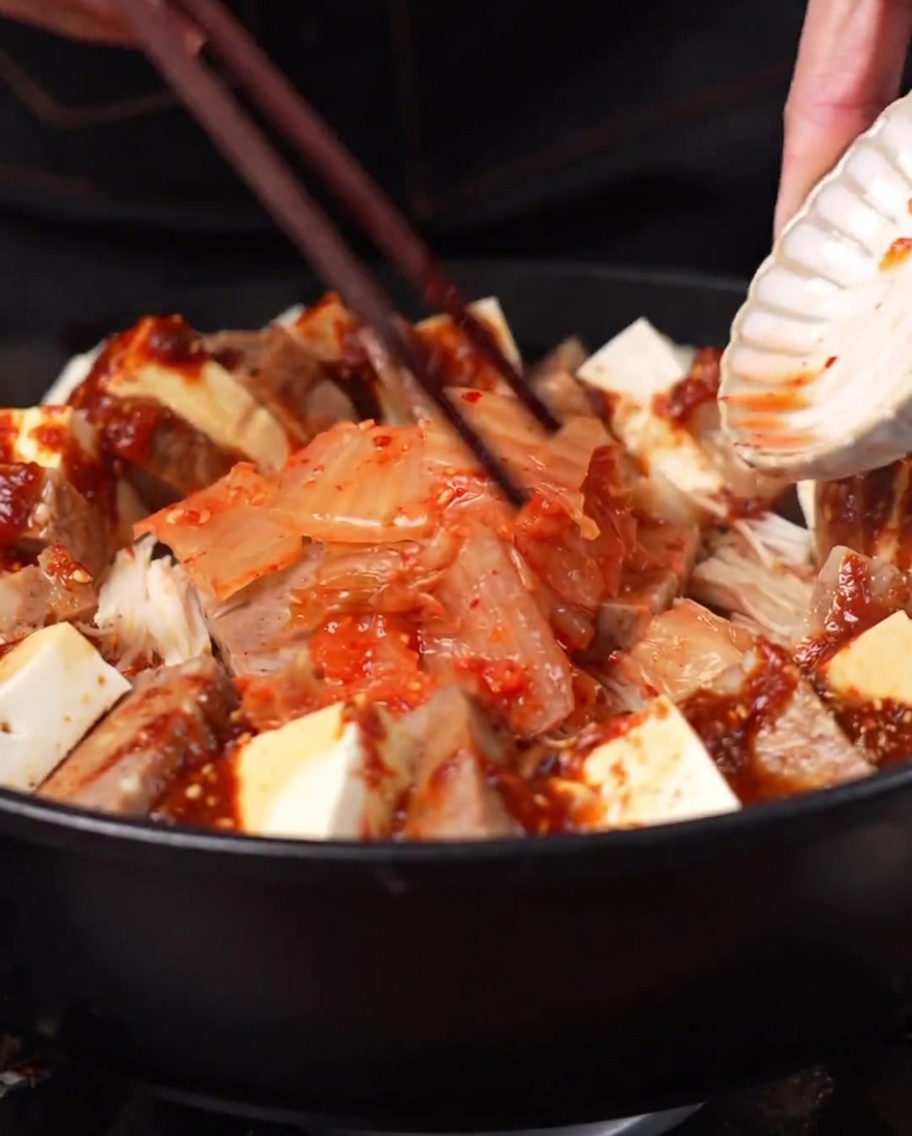 Una porzione di kimchi aggiunta al centro della pentola circondata dagli altri ingredienti.