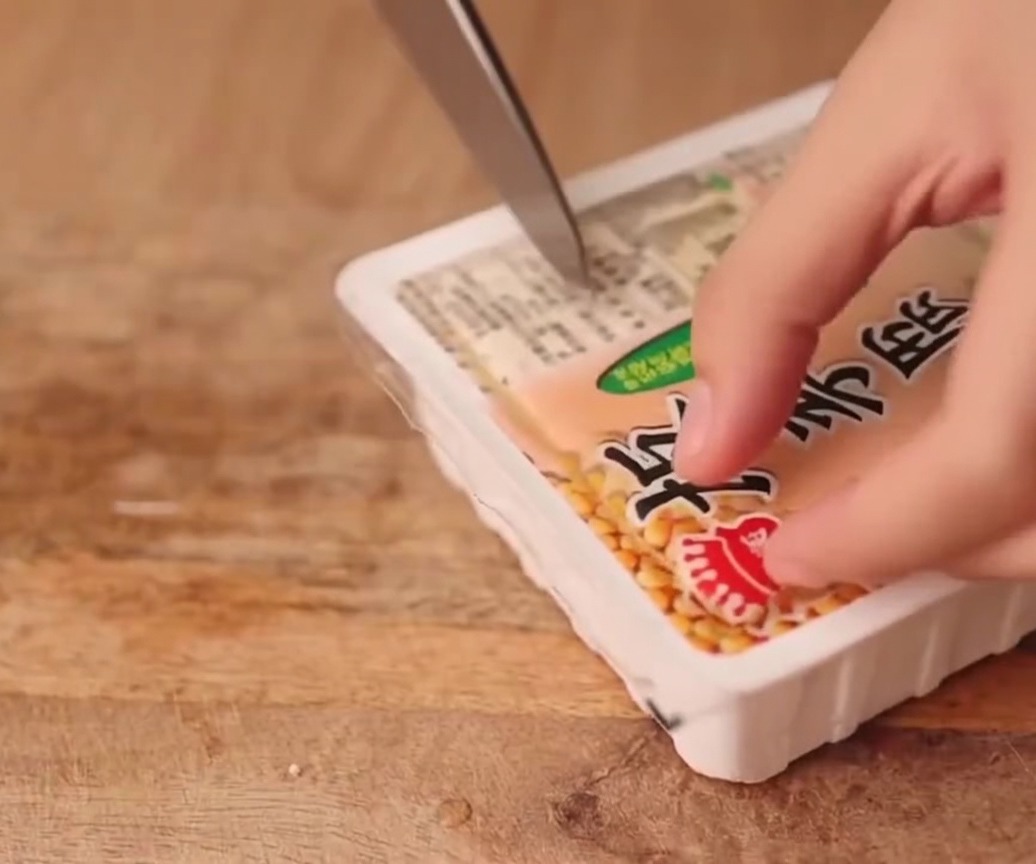 Un panetto di tofu compatto tagliato in fette uniformi su un tagliere di legno.