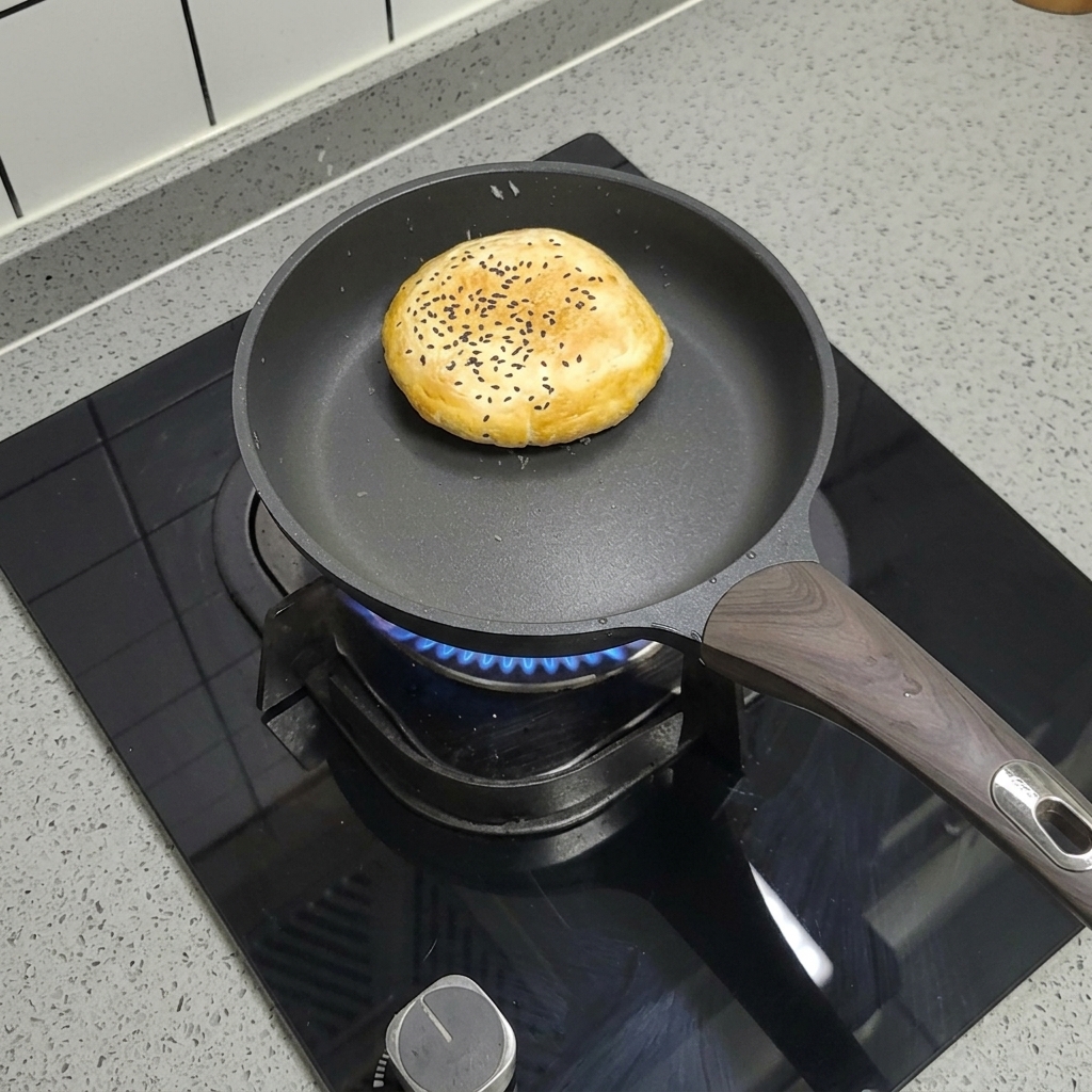 Un panino per hamburger surgelato con semi di sesamo che cuoce in una padella antiaderente asciutta.