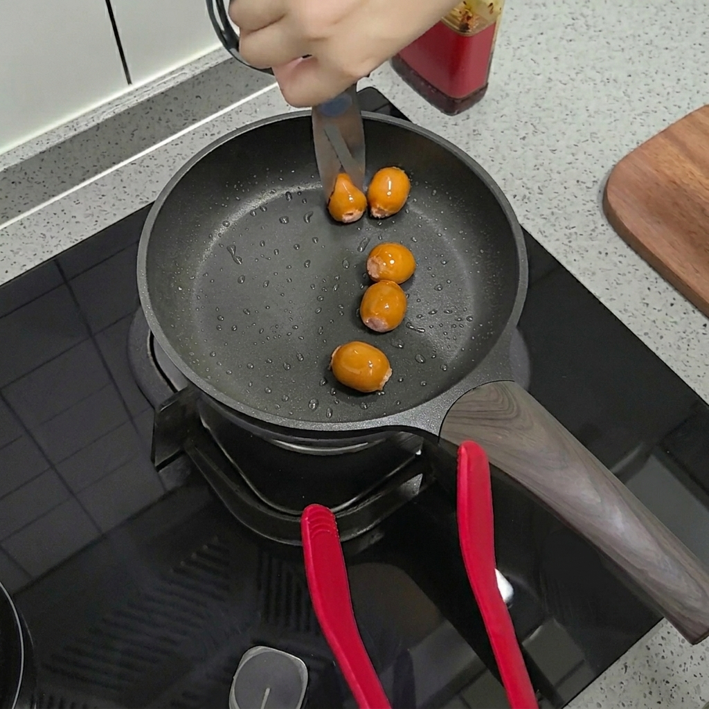 Forbici che tagliano salsicce già rosolate direttamente nella padella.