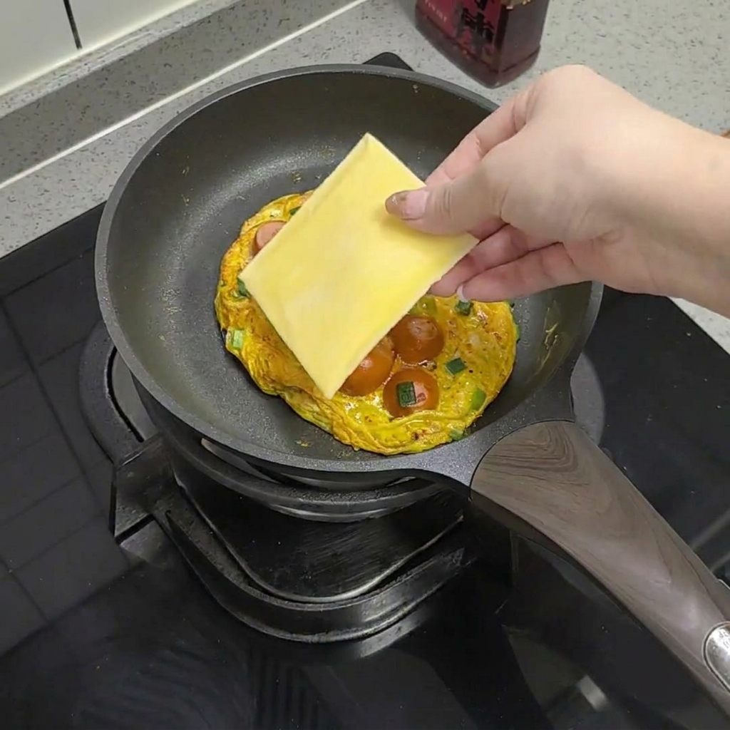 Una fetta di formaggio appoggiata sopra la frittata con salsicce.
