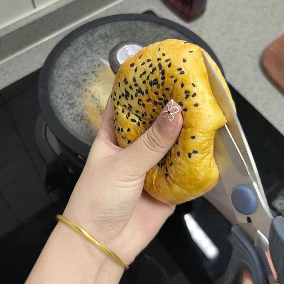 Primo piano di una mano che usa forbici da cucina per tagliare il panino tostato a metà.