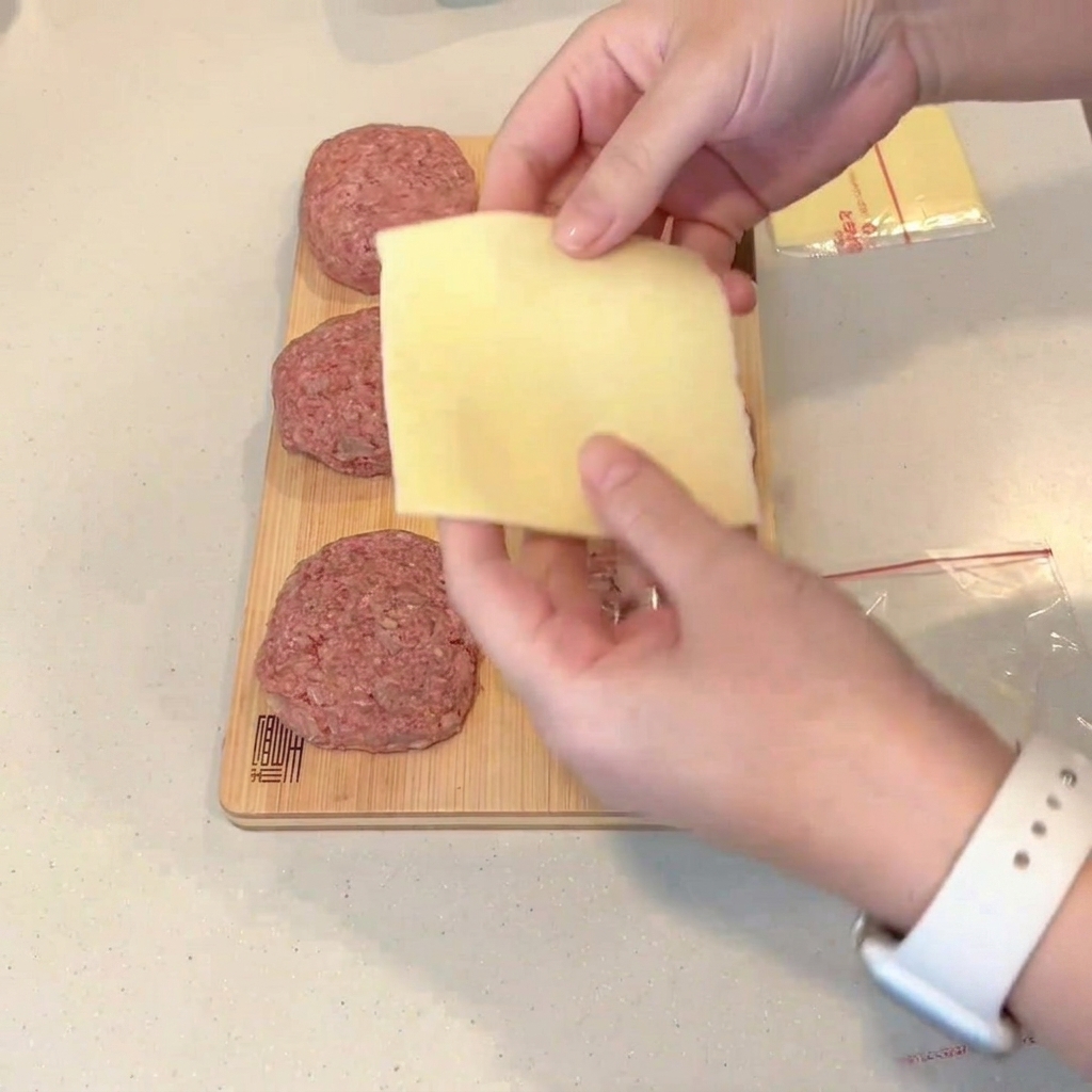 Una fetta di formaggio ripiegata posta al centro di un hamburger di carne cruda schiacciato.