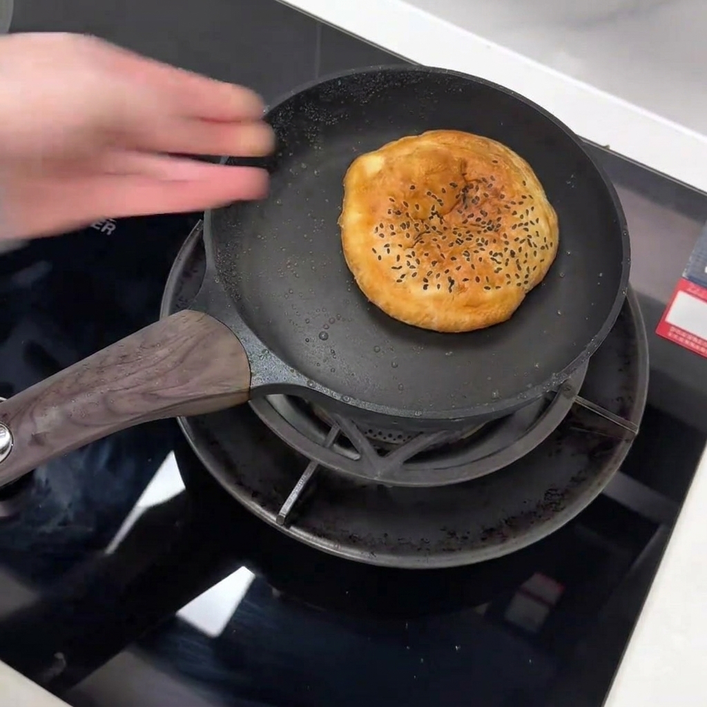 Una mano che mette un panino al sesamo nero in una padella antiaderente scura.
