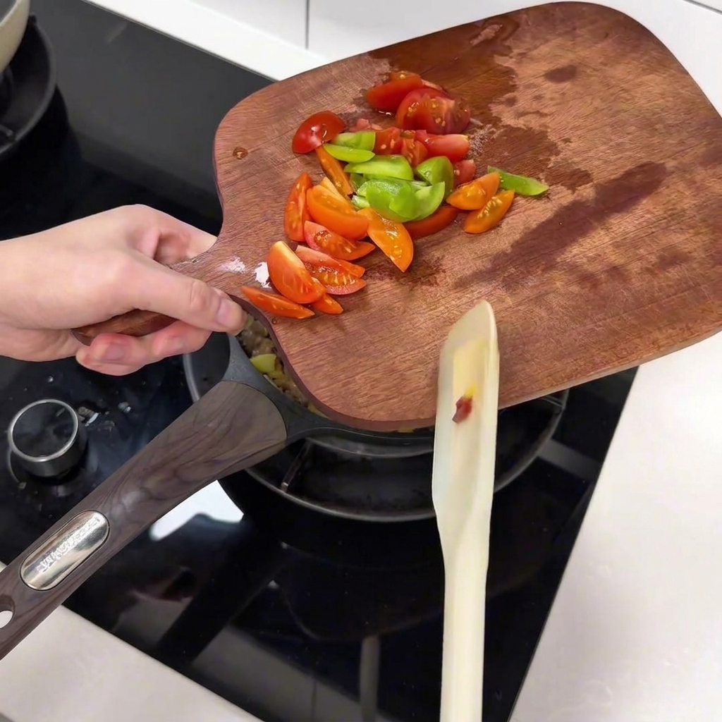 Pomodorini affettati e peperoni verdi trasferiti da un tagliere in una padella.