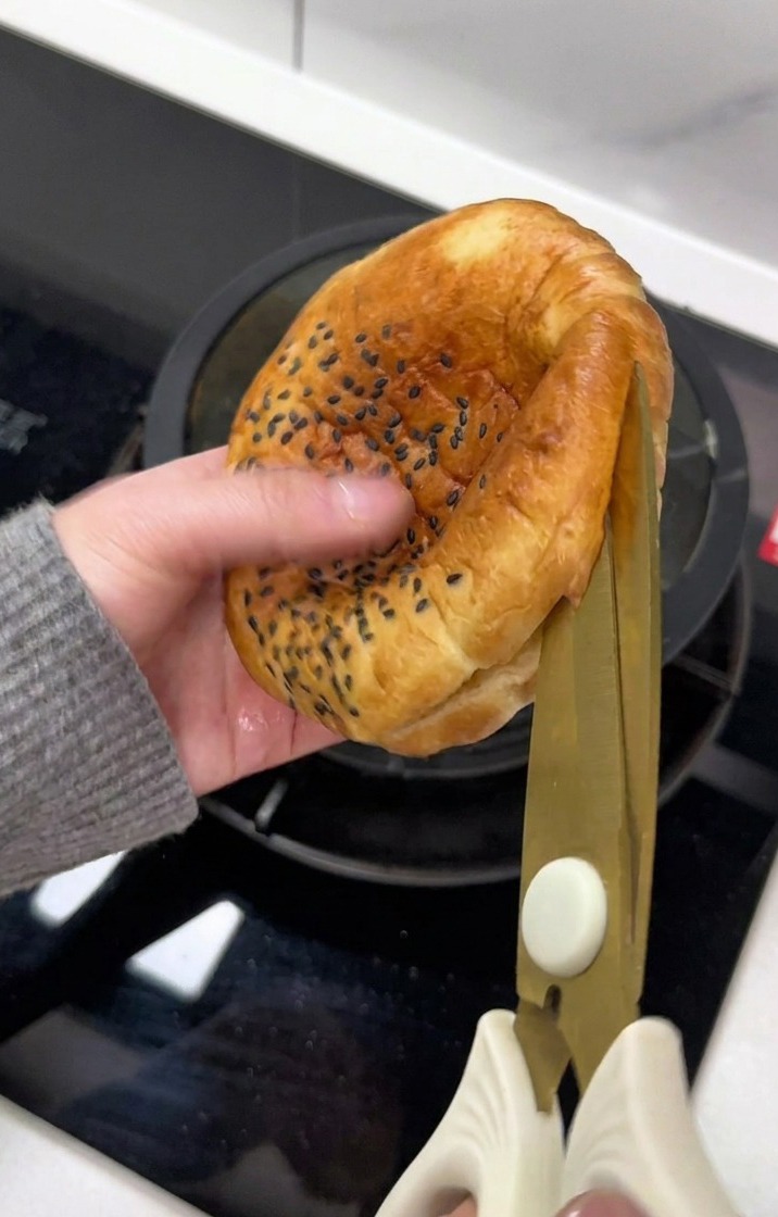 Una mano che usa le forbici per tagliare un panino al sesamo.