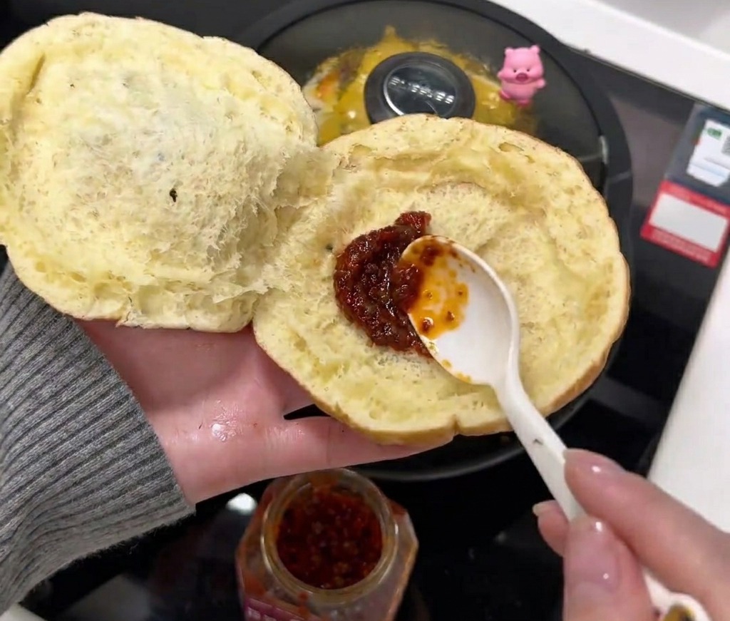 Un cucchiaio di salsa piccante spalmato sul lato interno di un panino aperto.