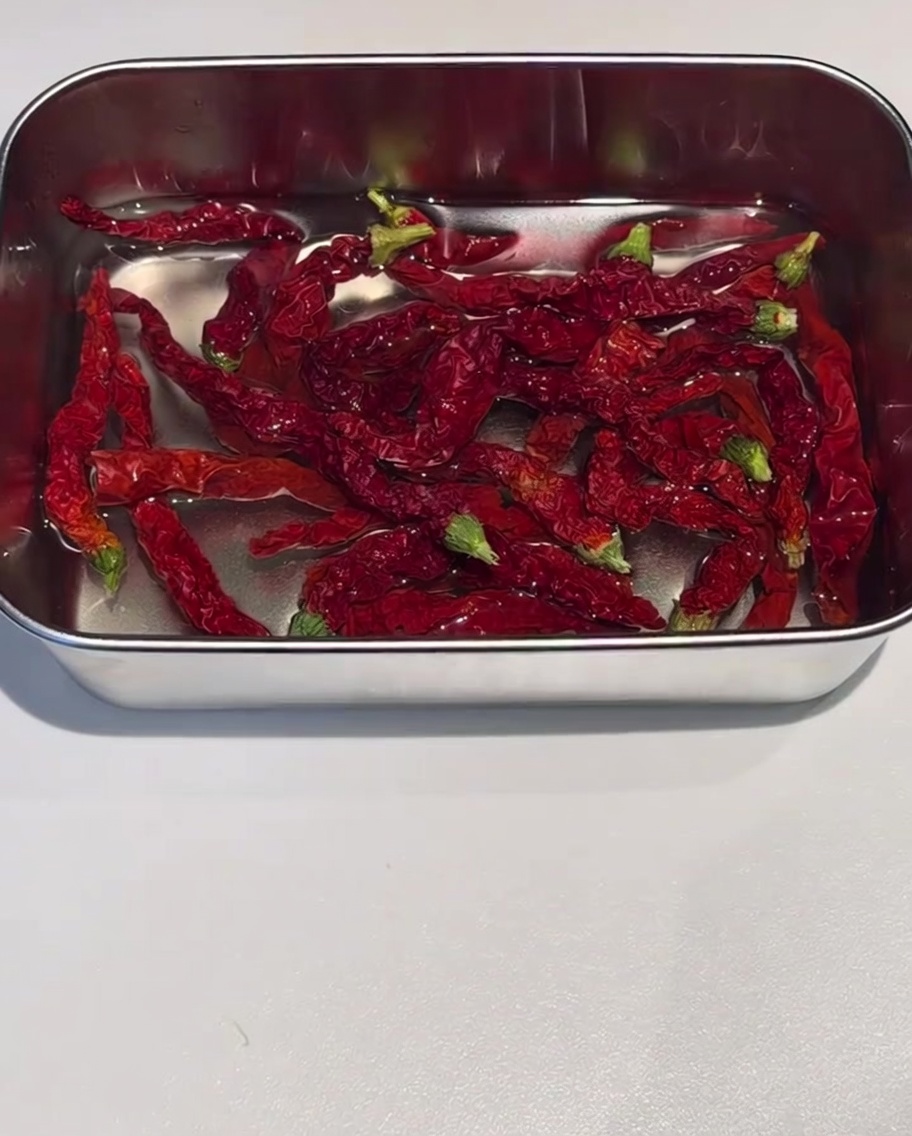 Bucce di peperoncino rosso essiccato in ammollo in un contenitore dacciaio con acqua calda.