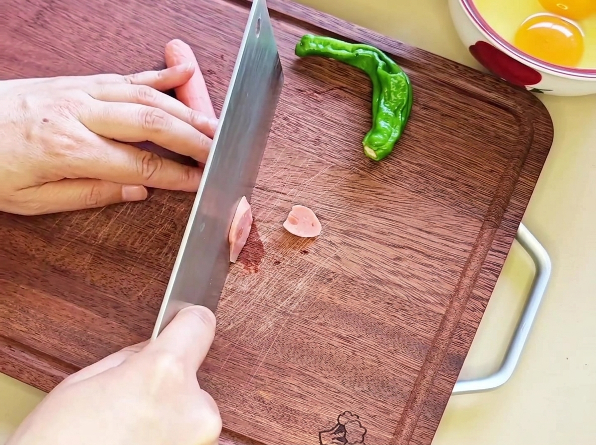 Fette diagonali di salsiccia disposte ordinatamente su un tagliere di legno, pronte per il passaggio successivo.