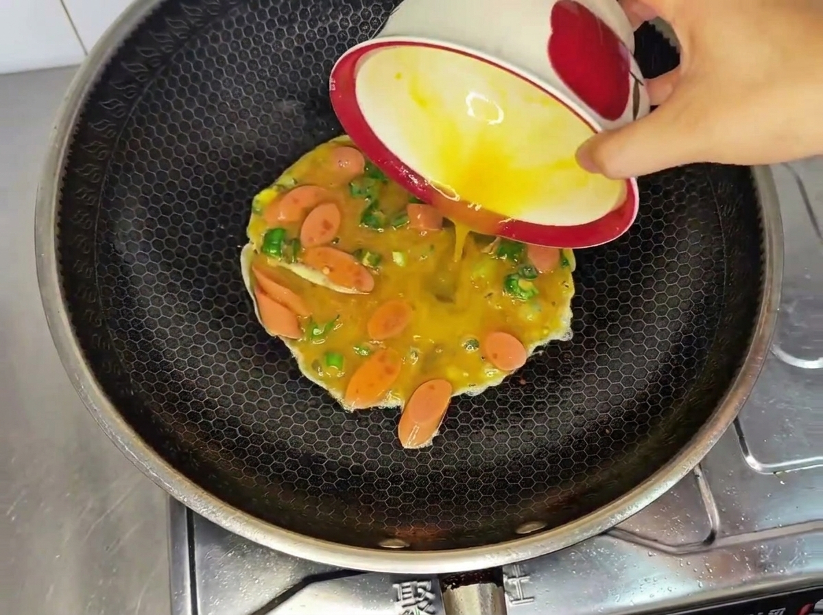 Il composto di uova sbattute, salsiccia e peperoncini versato in un wok caldo.