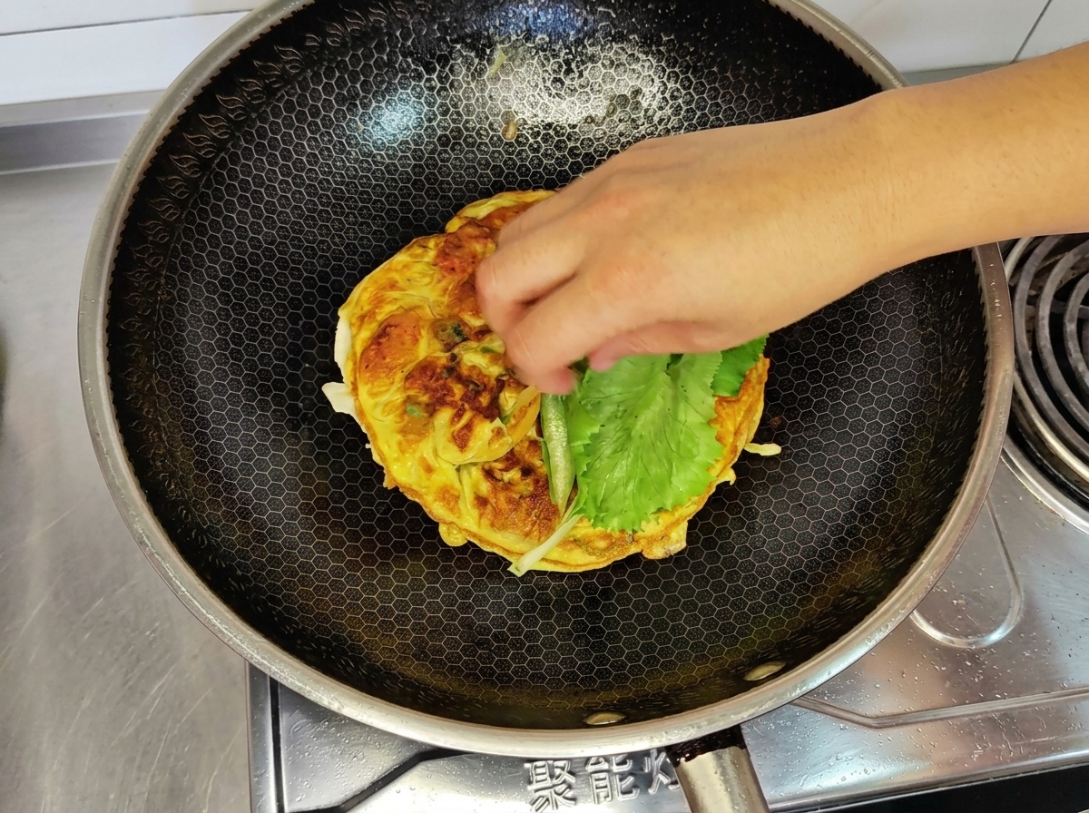 Una mano posiziona una foglia di lattuga verde fresca sopra lomelette cotta in padella.