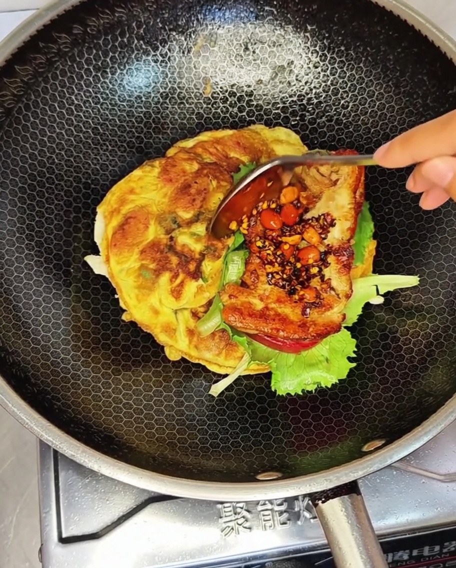 Un hamburger di pollo fritto condito con una cucchiaiata di salsa piccante alle arachidi sopra la lattuga in un wok.