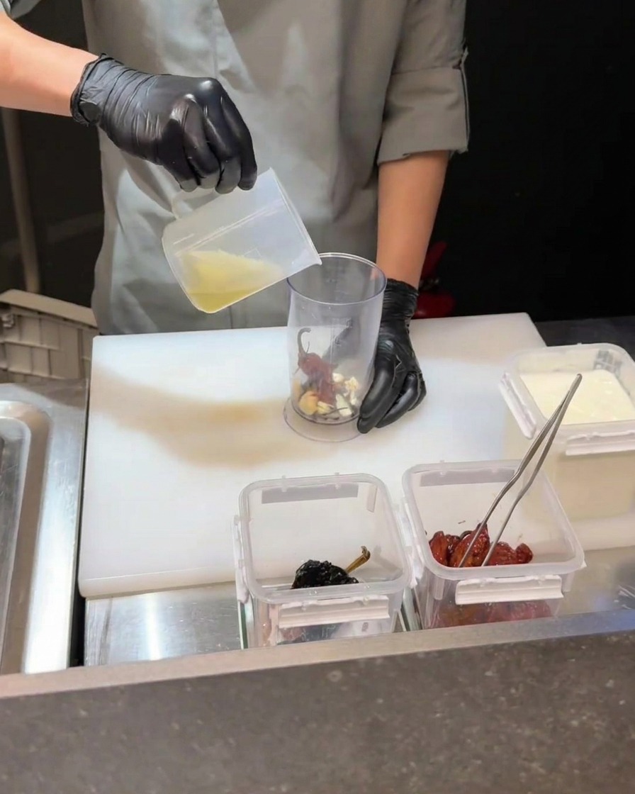 Frullatore a immersione che lavora peperoncini, tuorlo duovo e liquidi in un contenitore.