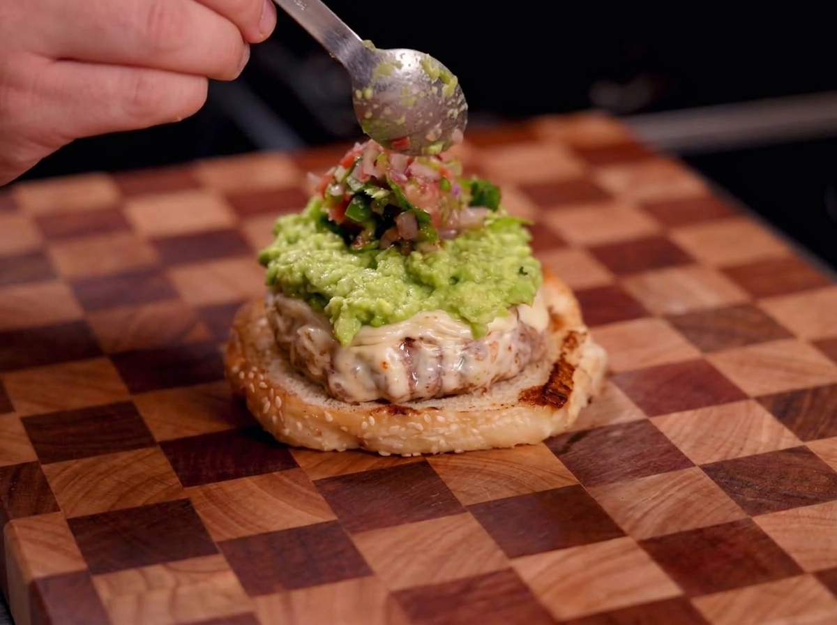 Una mano che usa un cucchiaio per aggiungere salsa rossa fresca sopra uno strato di guacamole.