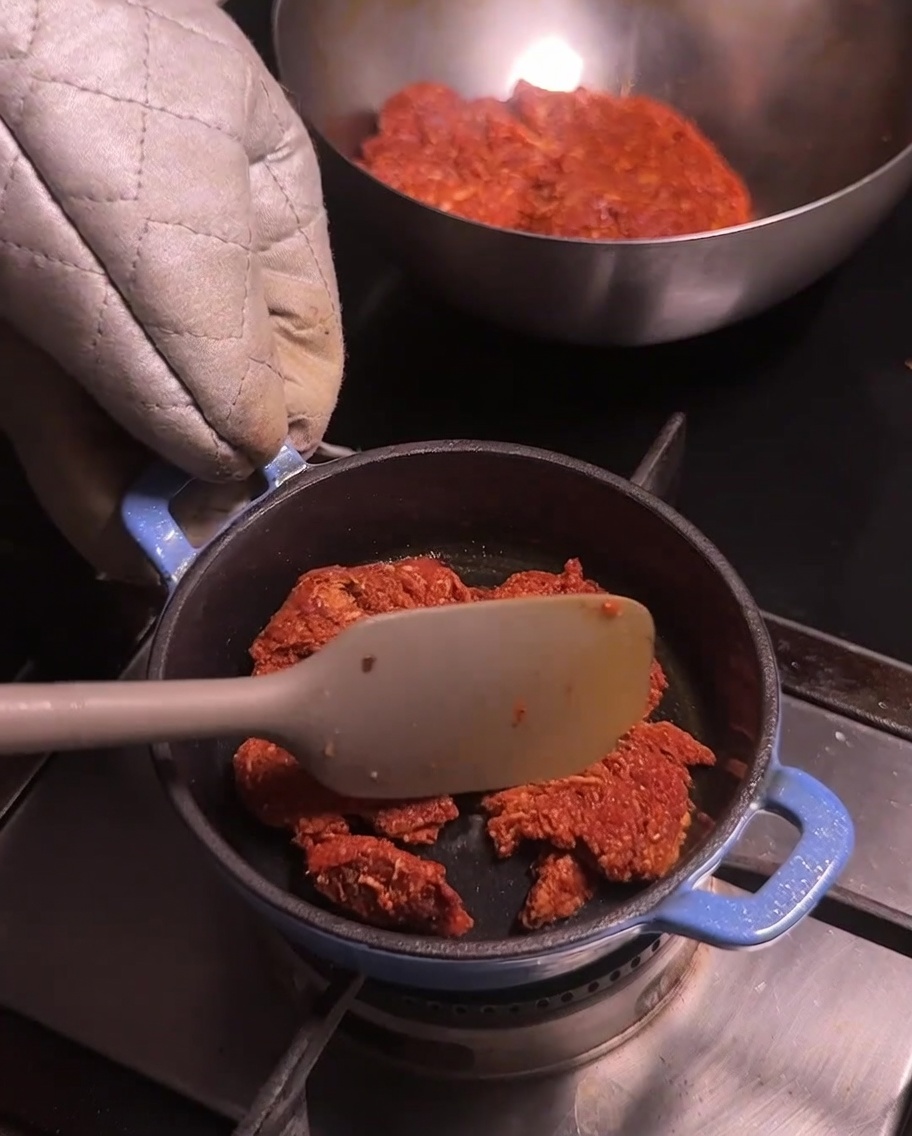 Una piccola pentola blu su un fornello con carne di maiale chorizo sbriciolata che viene mescolata con una spatola di colore chiaro.
