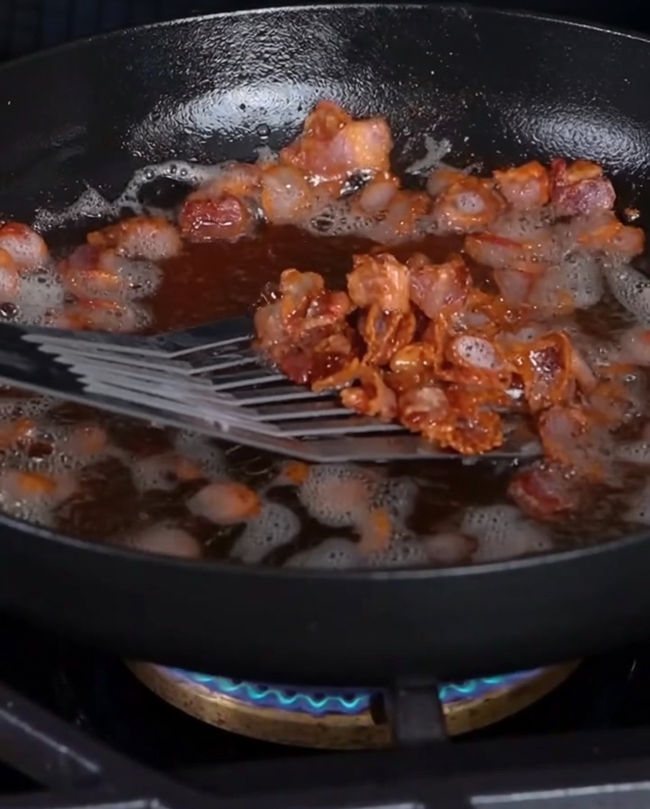 Pezzi di bacon croccanti sollevati dalla padella con una spatola forata.