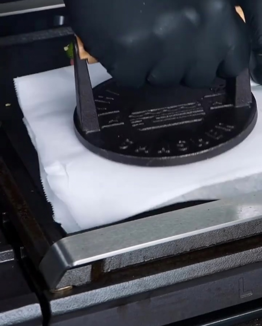 Un pressa-hamburger in ghisa che preme su un foglio di carta forno sopra un hamburger sulla piastra.