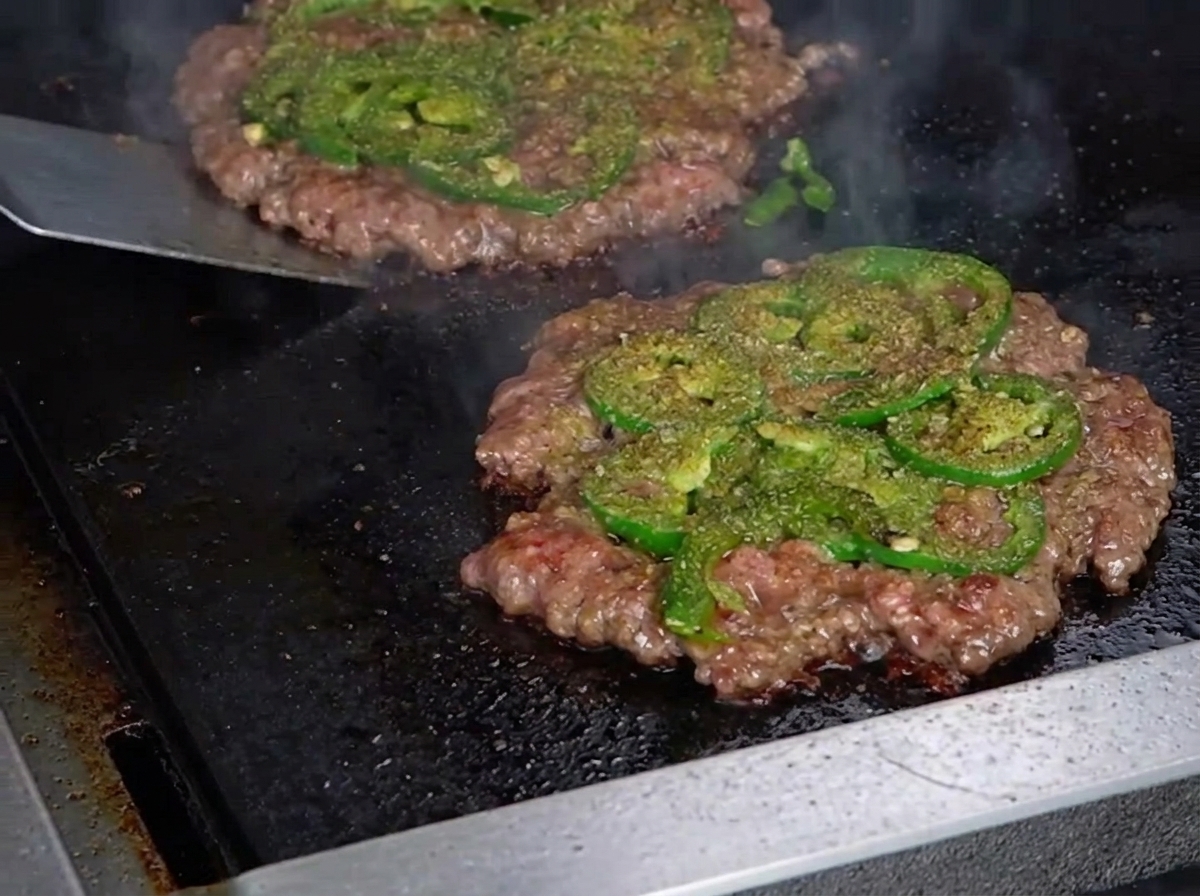 Una spatola di metallo che gira un sottile hamburger, rivelando una crosticina croccante sul lato inferiore.