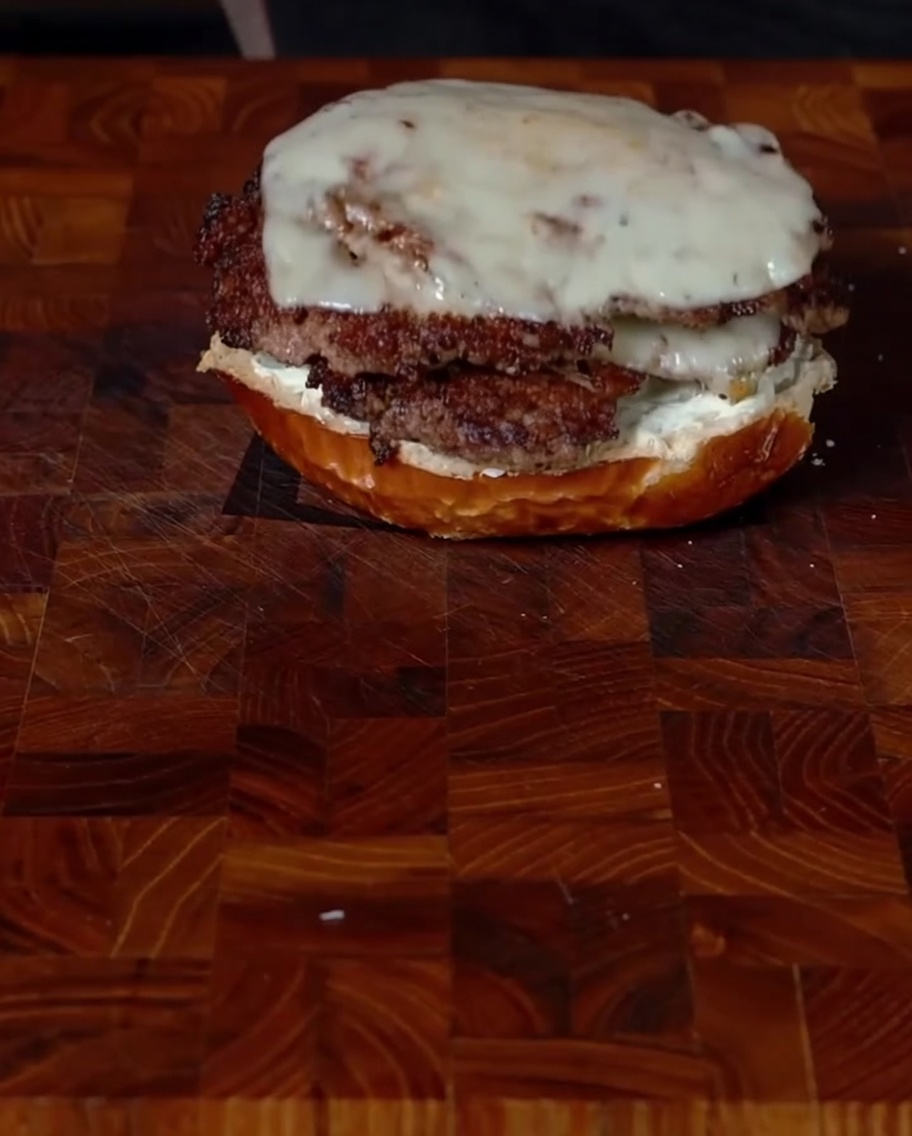 Posizionamento accurato di due polpette di burger con jalapeños e formaggio fuso sopra la base del panino.
