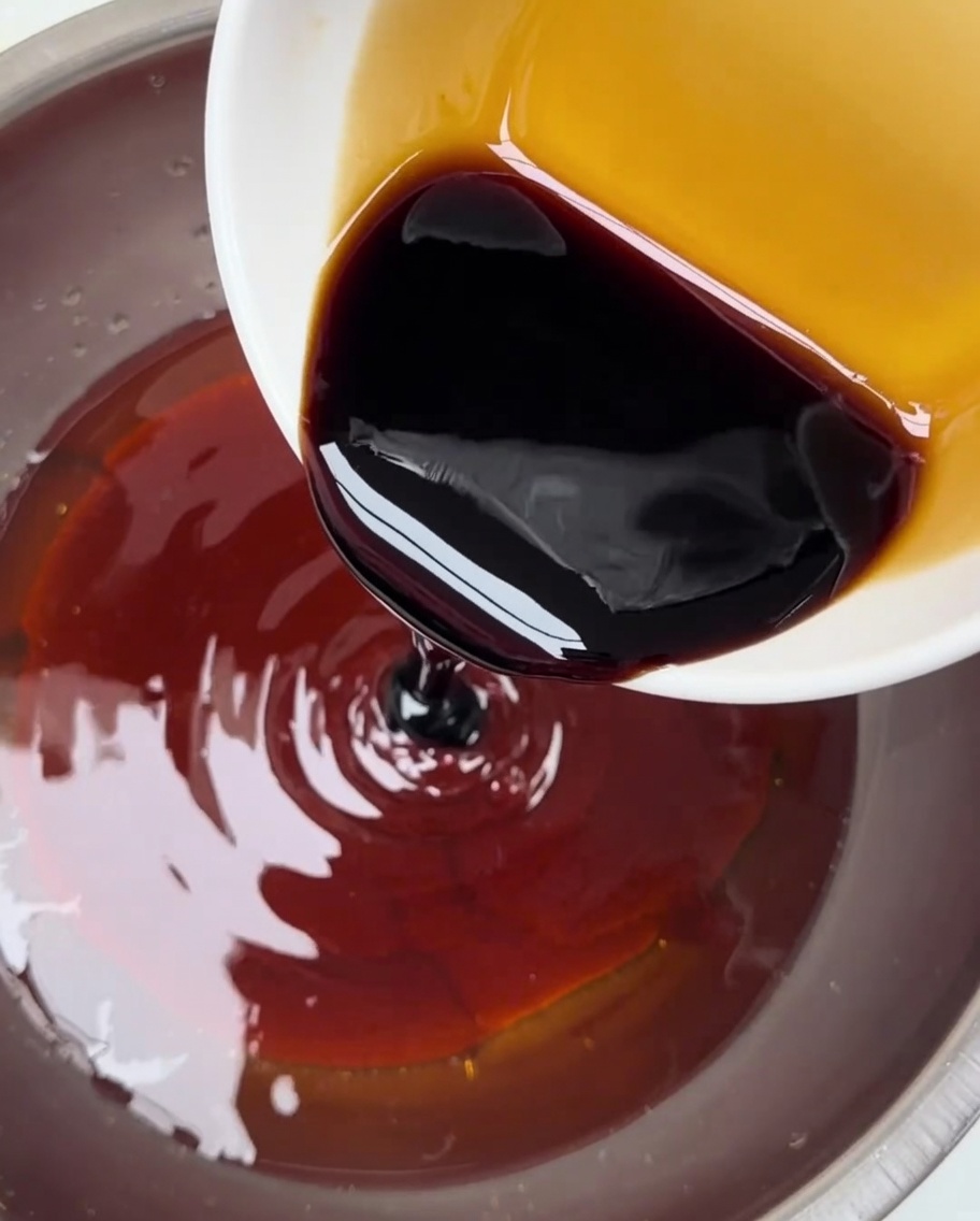 Salsa di soia scura versata da una ciotolina in un contenitore più grande contenente la miscela di pasta di peperoncino rossa.